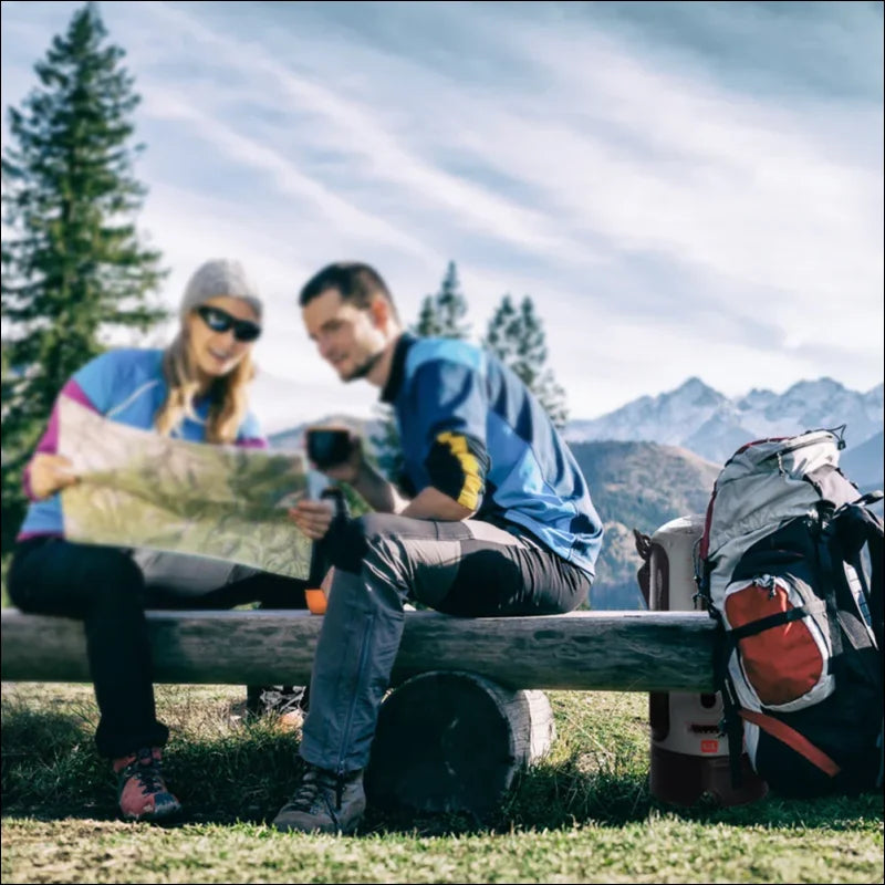 Zwei wanderer, die auf einer holzbank sitzen und eine karte studieren, mit rucksäcken in der nähe und bergen im hintergrund.