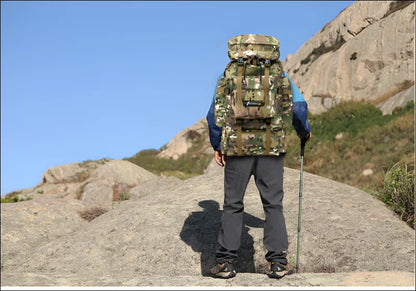 Wanderer mit tarnrucksack und trekkingstock auf felsigem gelände.