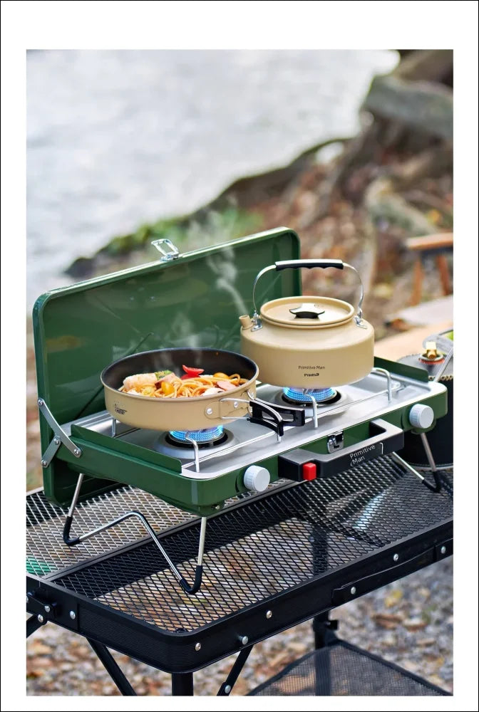 Tragbarer campingkocher mit einer pfanne mit essen und einem wasserkocher darauf.